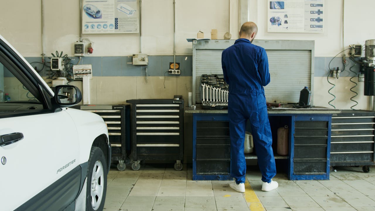services-02 Mechanic in blue overalls inspecting a white car in a well-equipped garage.