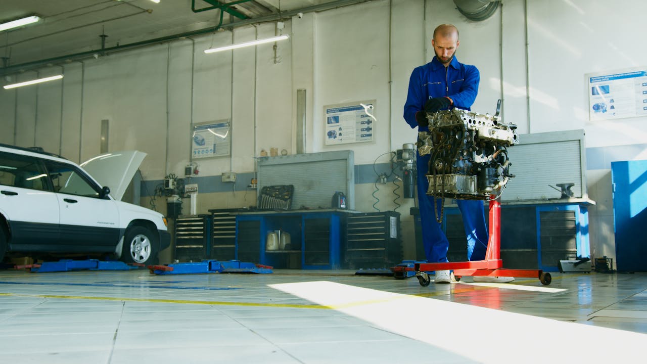 services-03 Mechanic lifting a car engine in a well-lit auto repair shop with vehicle in background.